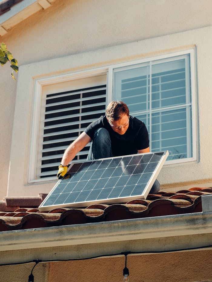 A worker installing a solar panel on a residential rooftop under bright sunlight.